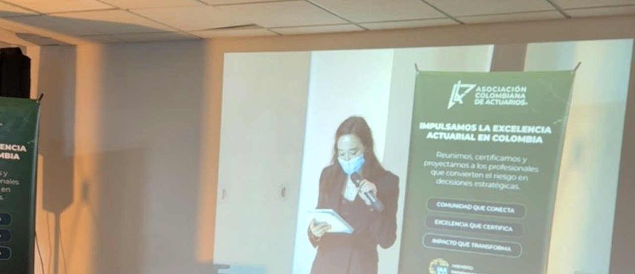 Participante remoto proyectado en sala durante asamblea mixta de la Asociacion Colombiana de Actuarios.