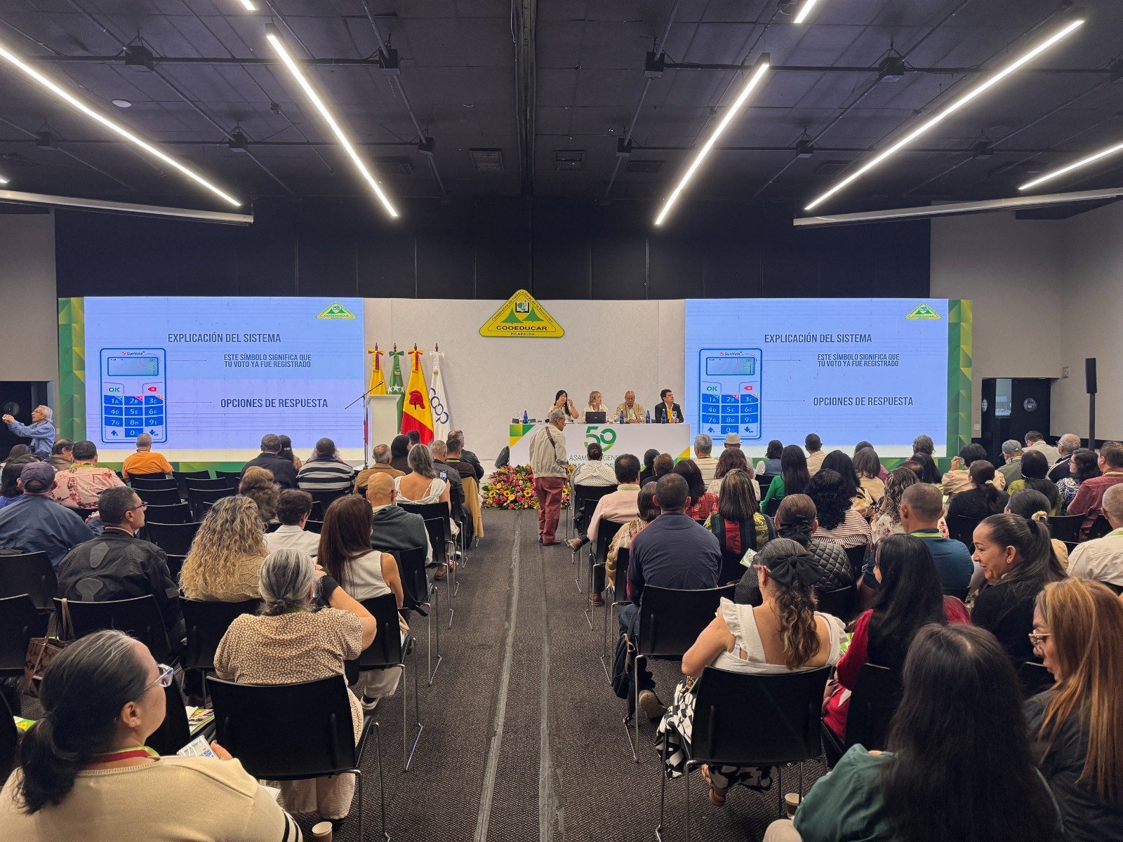 Asamblea Cooeducar 2026 en Pereira con pantallas, asistentes y sistema de votacion electronica con controles.