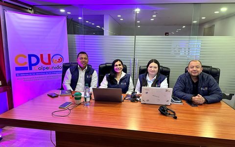 Mesa principal en montaje para asamblea Colpeunidos 2026 con laptops, iluminación y soporte de transmisión.